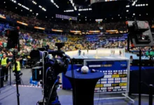 A professional camera setup captures a brightly lit indoor sports arena filled with spectators watching a game.