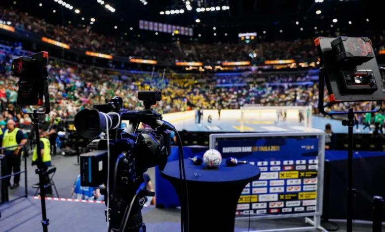 A professional camera setup captures a brightly lit indoor sports arena filled with spectators watching a game.